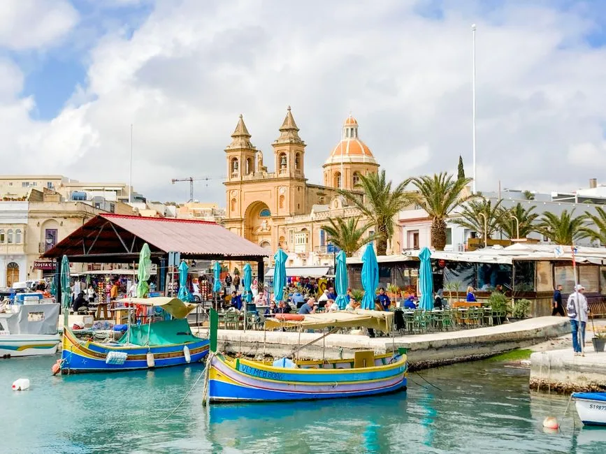 몰타 Marsaxlokk의 알록달록한 어선과 활기찬 시장, 배경에는 역사적인 교회